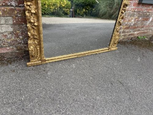 A large nineteenth-century carved giltwood overmantel mirror featuring a prominent central urn crest and floral mouldings. View V