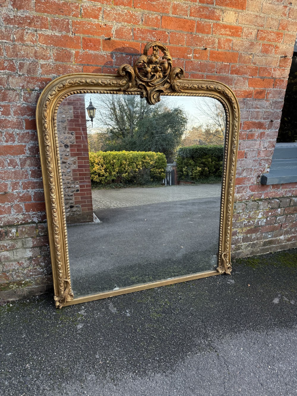 A large 19th-century English giltwood overmantel mirror featuring an arched frame decorated with beaded moulding and a carved rococo top crest.