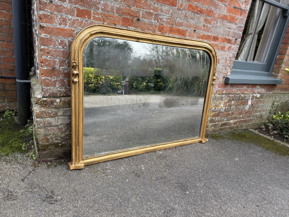 A large 19th-century arched gilt overmantel mirror featuring a moulded frame with gesso floral mouldings near the lower sides.