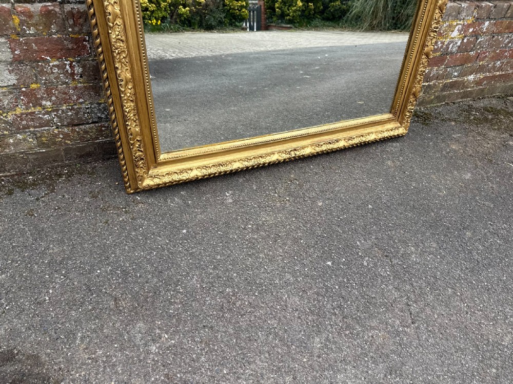 A large rectangular 19th-century wall mirror featuring a gilded wood and gesso frame decorated with a carved ribbon crest at the top. View V