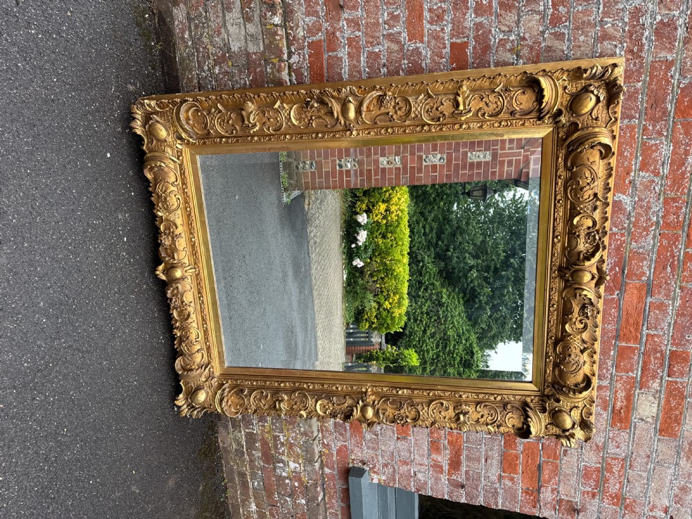 A large rectangular nineteenth-century wall mirror set in a thick frame carved with ornate gold gilded gesso scrollwork. View VII