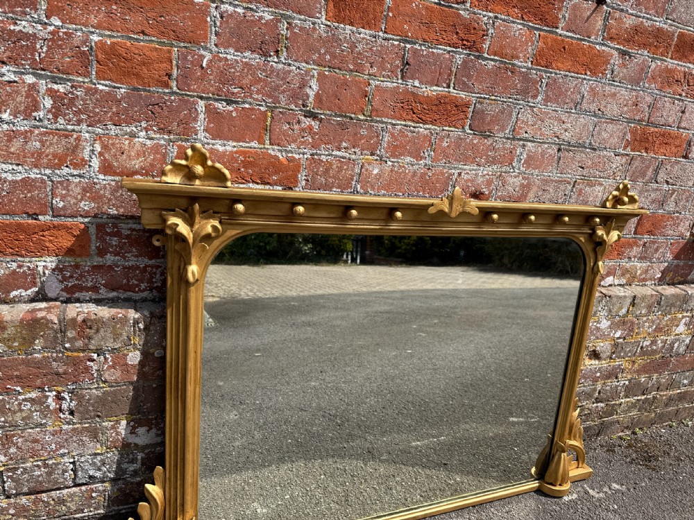 A 19th-century English giltwood and gesso overmantel mirror featuring detailed acanthus leaf carving and ball moulding along the upper frame. View II