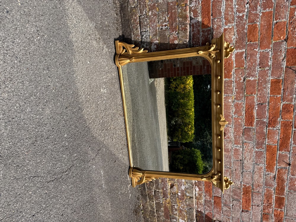 A 19th-century English giltwood and gesso overmantel mirror featuring detailed acanthus leaf carving and ball moulding along the upper frame. View VI