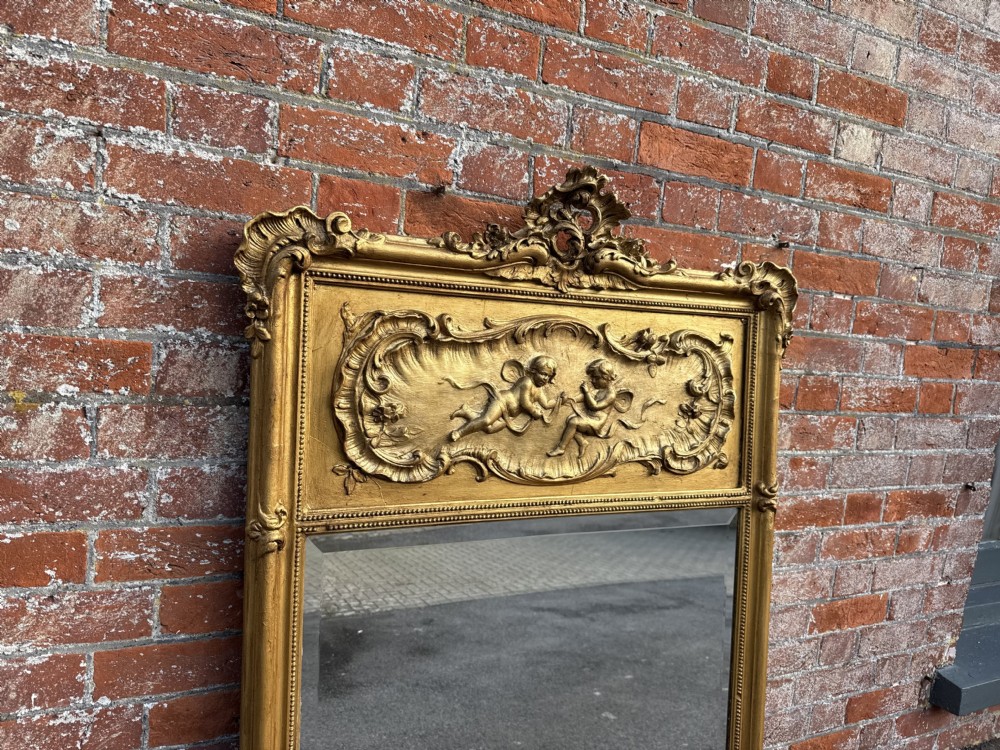 A large 19th-century French gilt wood and gesso mirror featuring a carved cherub frieze panel and an ornate crested top. View VI