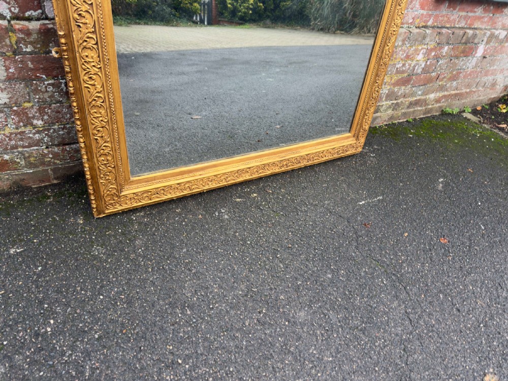 A large rectangular 19th-century English giltwood wall mirror featuring an ornate carved gesso frame with foliate moulding and a gold leaf finish. View II
