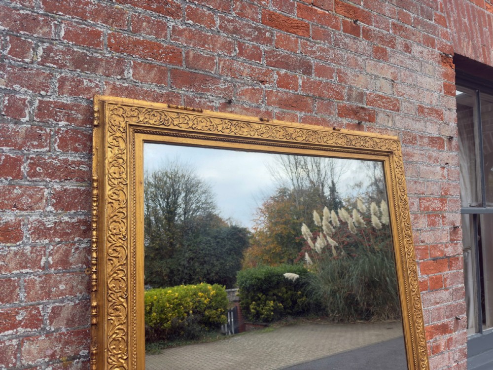 A large rectangular 19th-century English giltwood wall mirror featuring an ornate carved gesso frame with foliate moulding and a gold leaf finish. View V