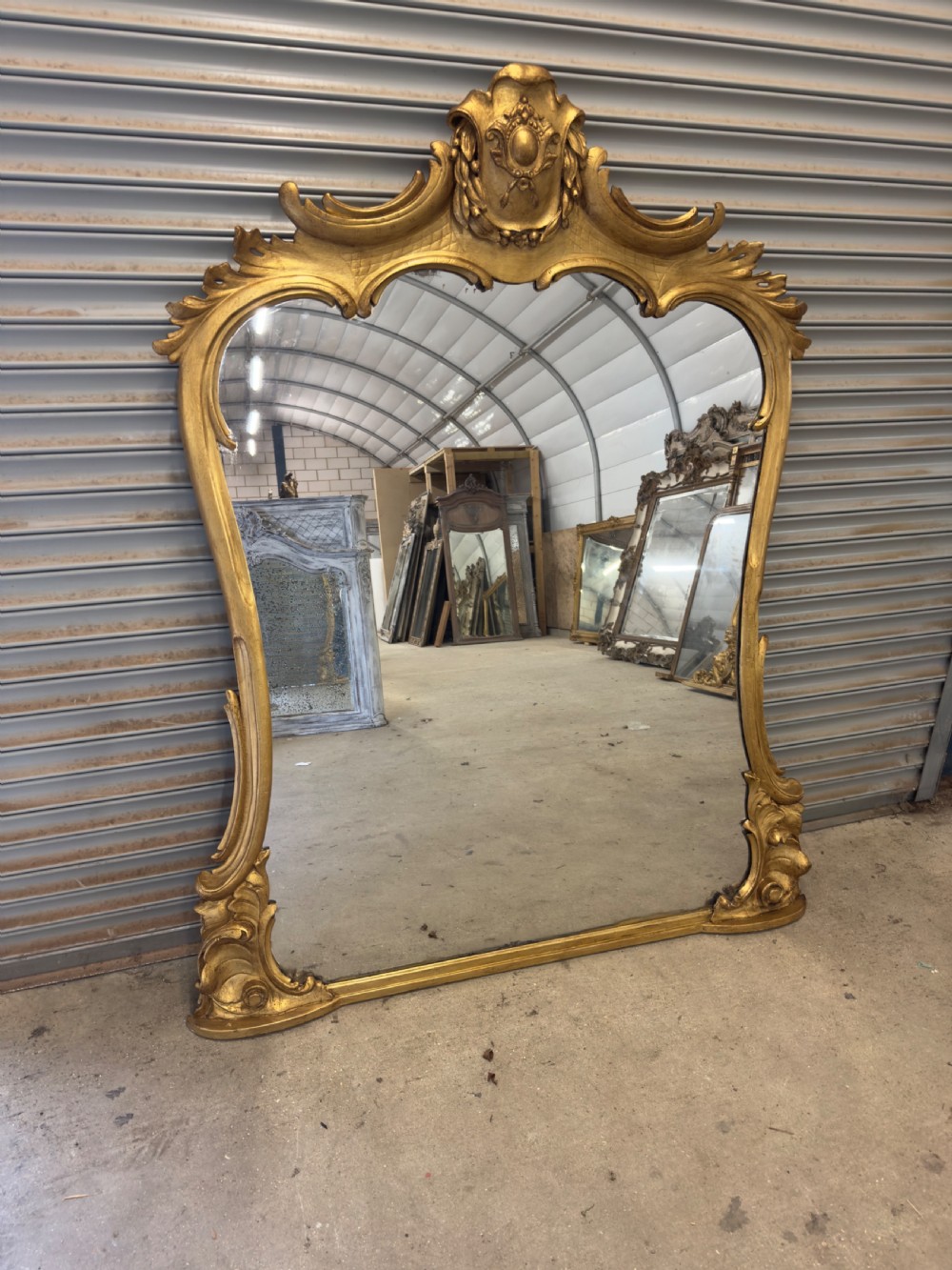 A large 19th-century giltwood overmantel mirror with an ornate carved cartouche crest and acanthus leaf scroll moulding.