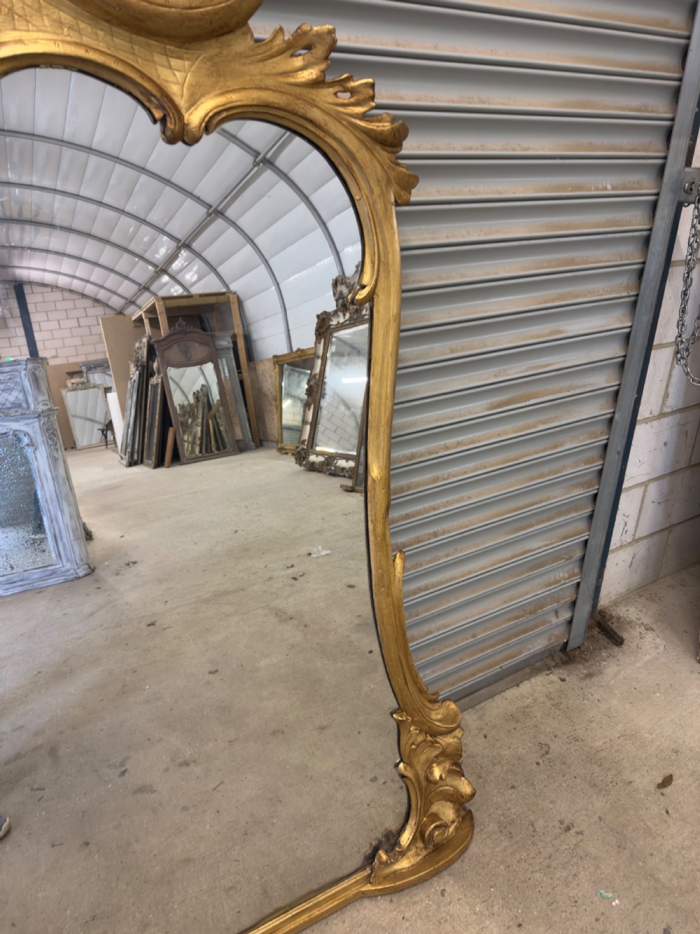 A large 19th-century giltwood overmantel mirror with an ornate carved cartouche crest and acanthus leaf scroll moulding. View V