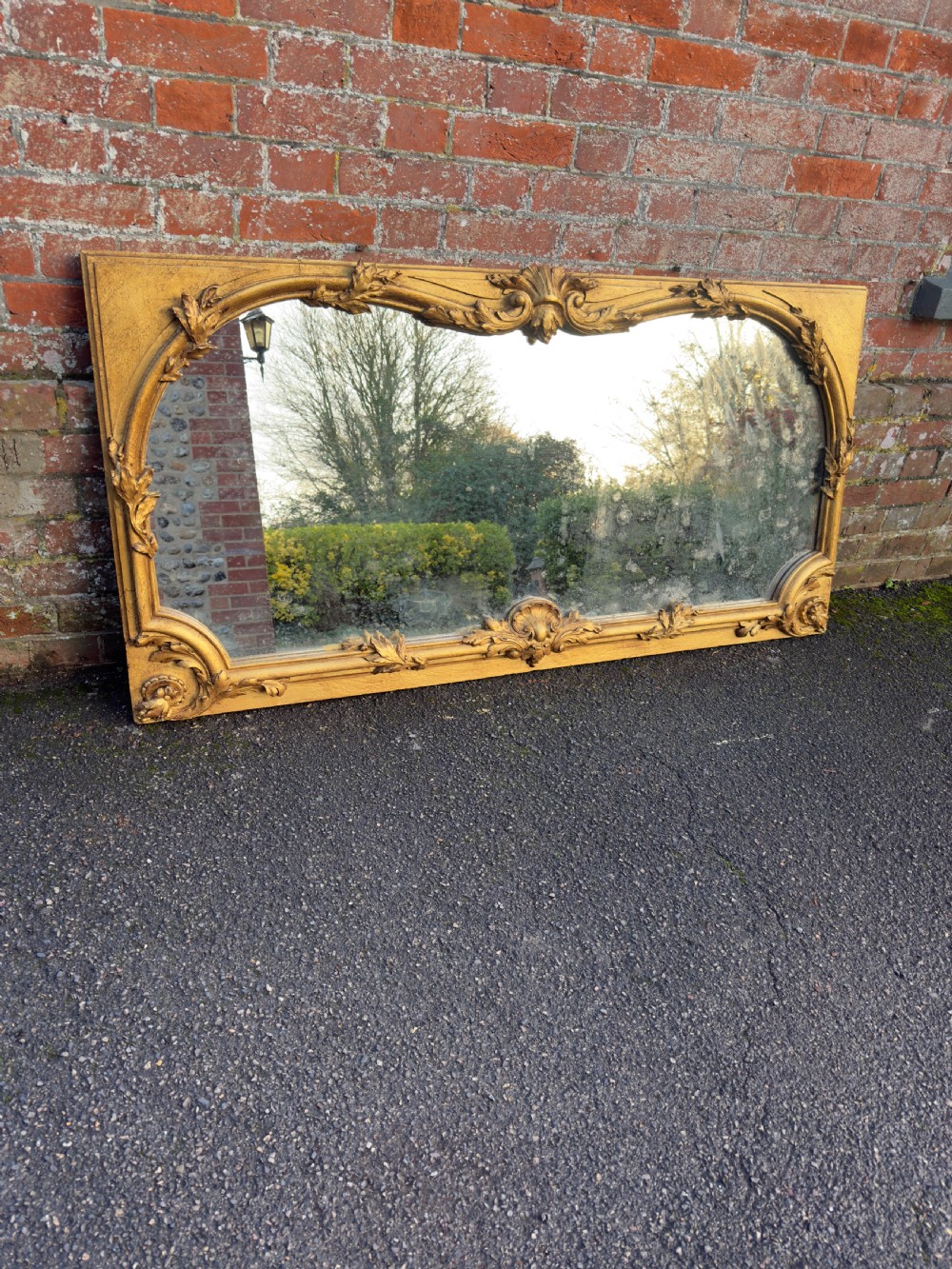 A large horizontal 19th-century overmantel mirror featuring a gilded wood and gesso frame with ornate carved acanthus leaf motifs.