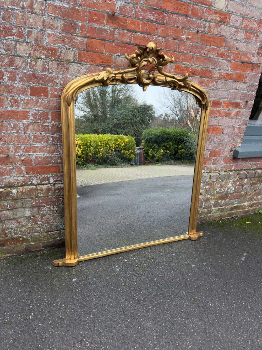 A large 19th-century giltwood overmantel mirror featuring an arched top adorned with a carved scroll and leaf cresting.