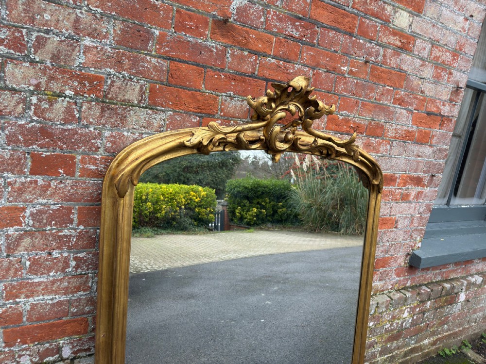 A large 19th-century giltwood overmantel mirror featuring an arched top adorned with a carved scroll and leaf cresting. View II
