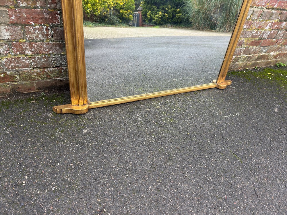 A large 19th-century giltwood overmantel mirror featuring an arched top adorned with a carved scroll and leaf cresting. View VII