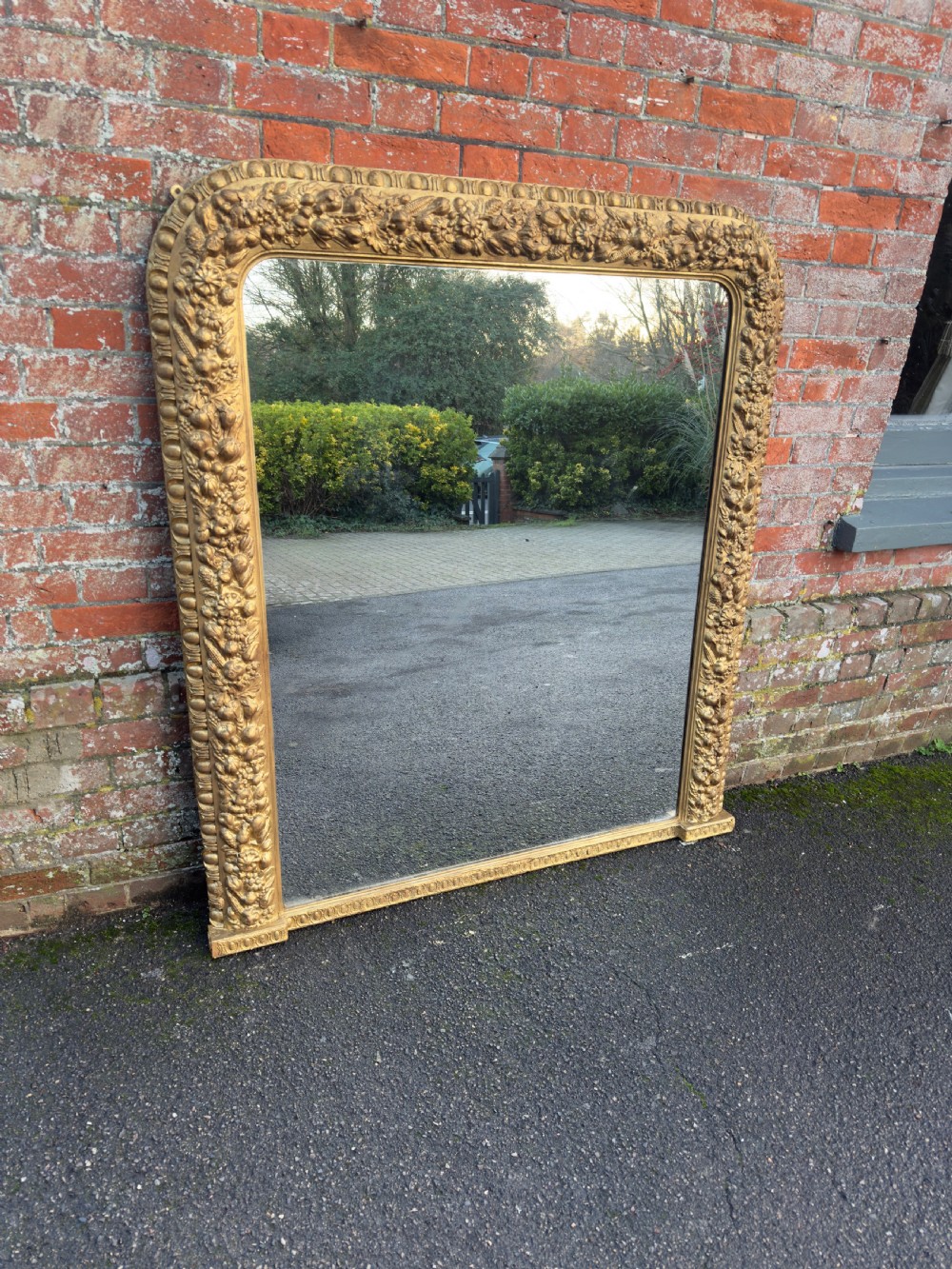 A large nineteenth-century Victorian giltwood and gesso overmantel mirror featuring an arched upper frame embellished with dense floral and fruit relief carvings.