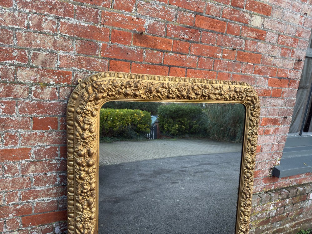A large nineteenth-century Victorian giltwood and gesso overmantel mirror featuring an arched upper frame embellished with dense floral and fruit relief carvings. View II