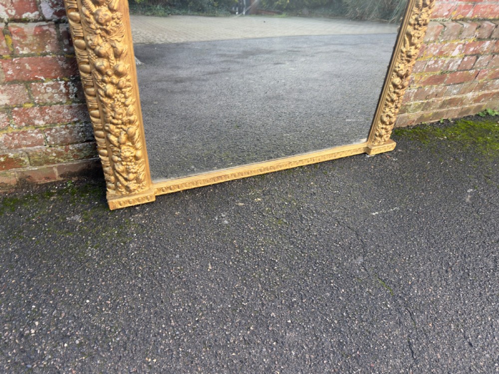 A large nineteenth-century Victorian giltwood and gesso overmantel mirror featuring an arched upper frame embellished with dense floral and fruit relief carvings. View IV