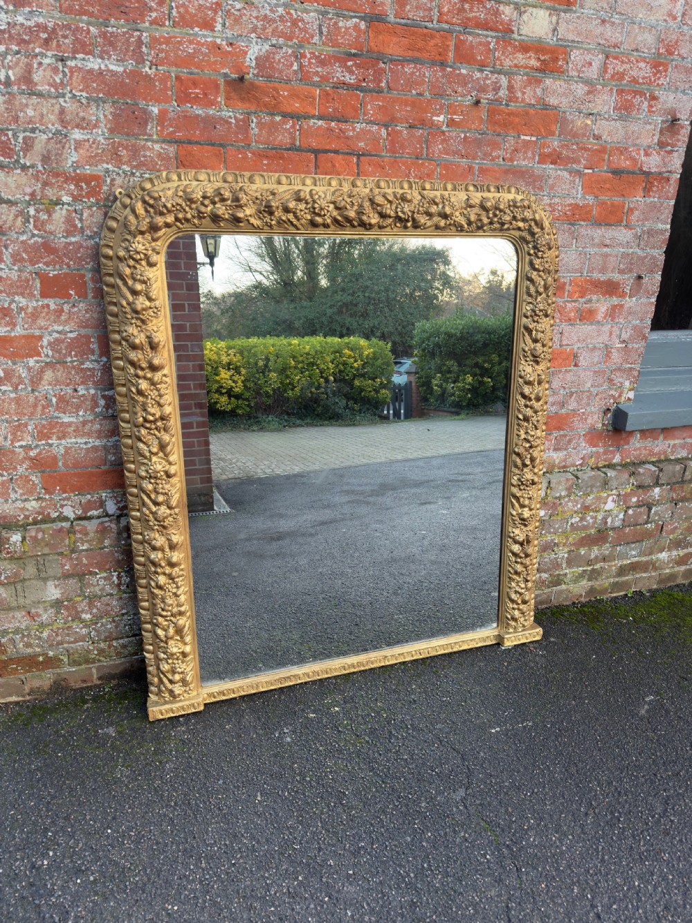 A large nineteenth-century Victorian giltwood and gesso overmantel mirror featuring an arched upper frame embellished with dense floral and fruit relief carvings. View VI