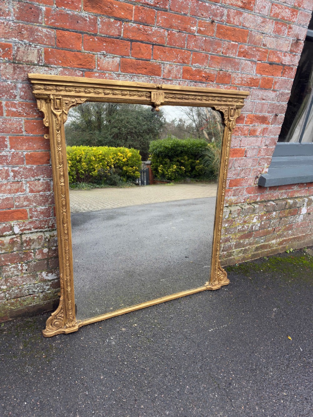 A large 19th-century rectangular overmantel mirror featuring a gilded gesso frame with floral moulding, scrolled side feet, and a stepped top cornice.