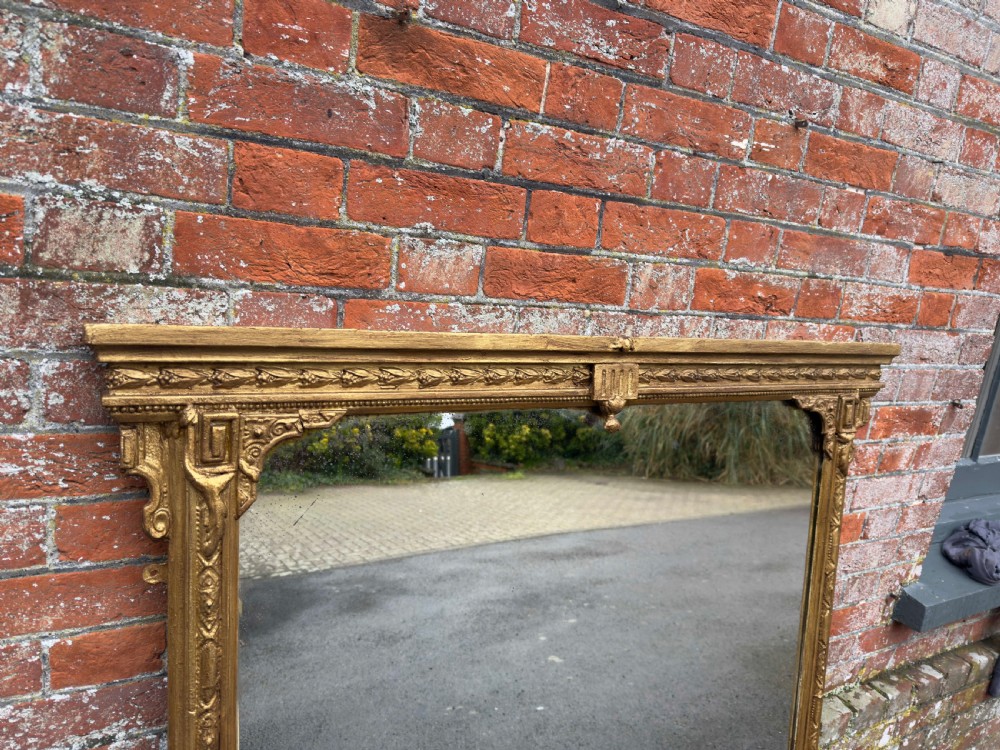 A large 19th-century rectangular overmantel mirror featuring a gilded gesso frame with floral moulding, scrolled side feet, and a stepped top cornice. View II