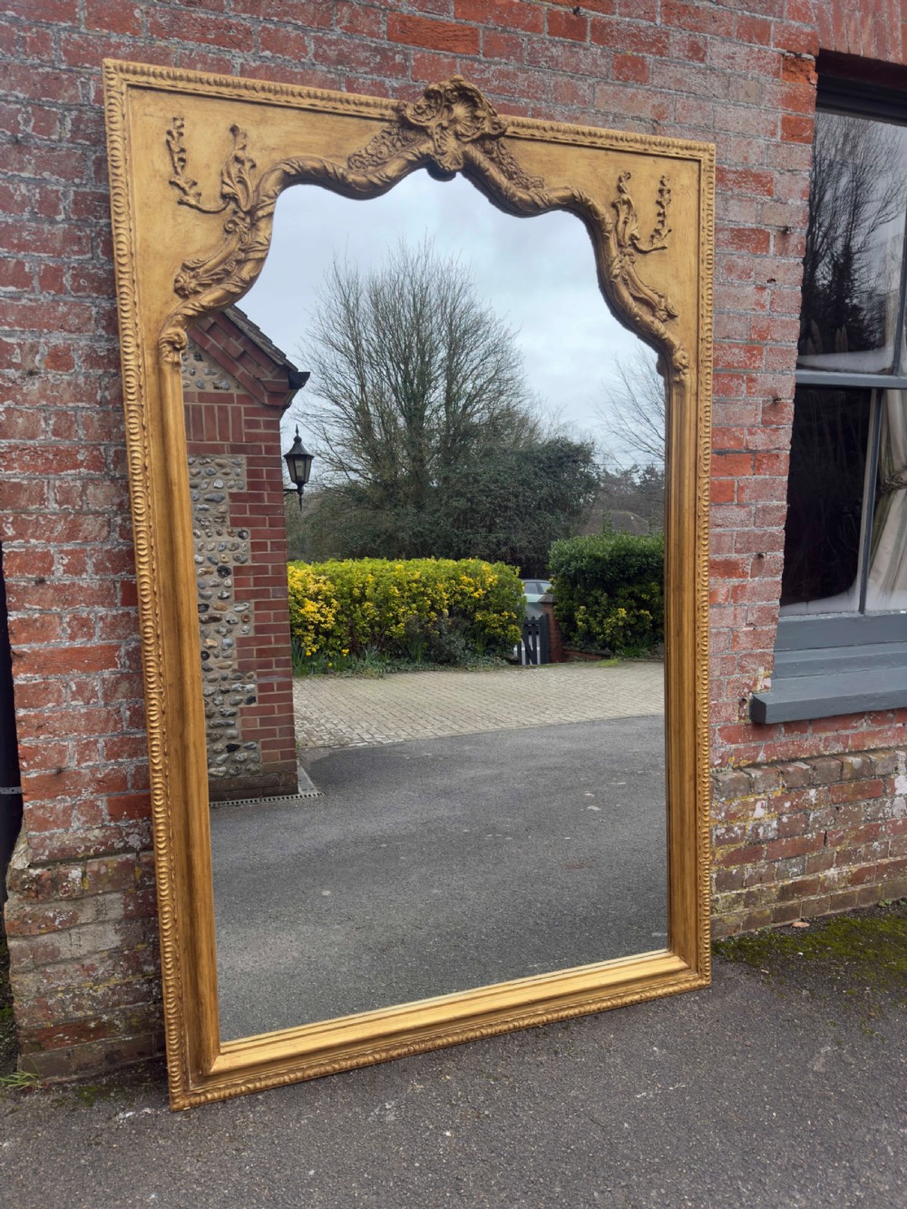 A large 19th-century English giltwood wall mirror with a shaped arched top and carved gesso detail.