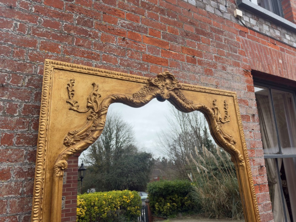 A large 19th-century English giltwood wall mirror with a shaped arched top and carved gesso detail. View III