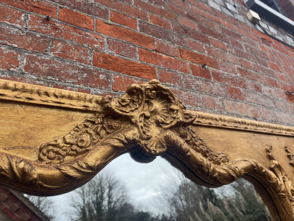A large 19th-century English giltwood wall mirror with a shaped arched top and carved gesso detail. View V