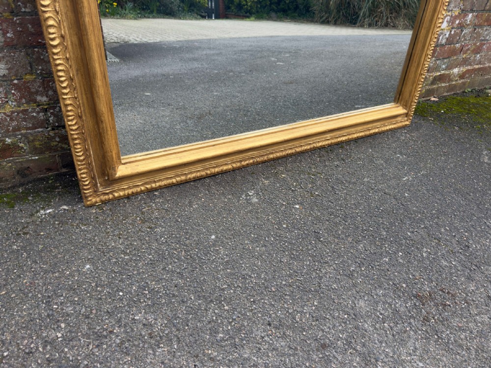 A large 19th-century English giltwood wall mirror with a shaped arched top and carved gesso detail. View VII