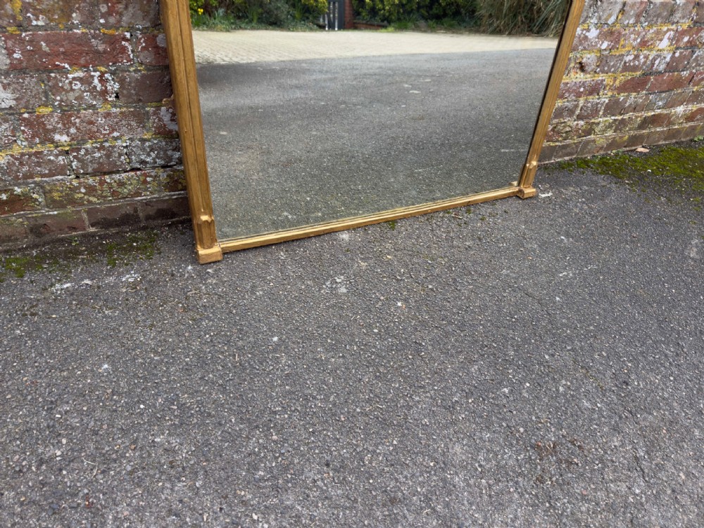 A large 19th-century rectangular giltwood overmantel mirror featuring a carved pediment with spindle detailing and foliate corner ornamentation. View III