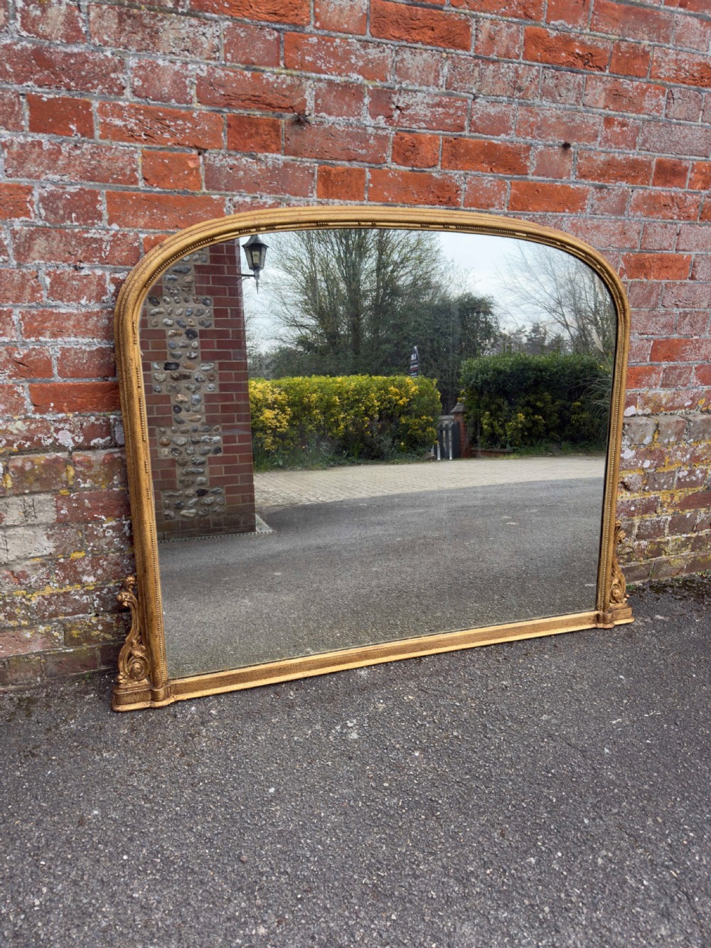 A large 19th-century English giltwood overmantel mirror featuring an arched top frame decorated with beaded moulding and carved scrollwork details at the base.