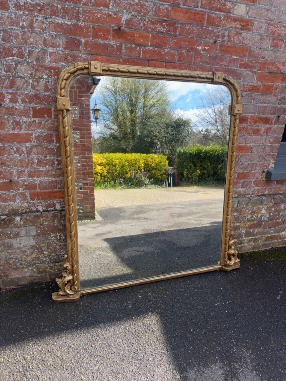 A large 19th-century English giltwood overmantel mirror featuring a carved rope twist frame with rounded top corners and acanthus leaf base scrolls.