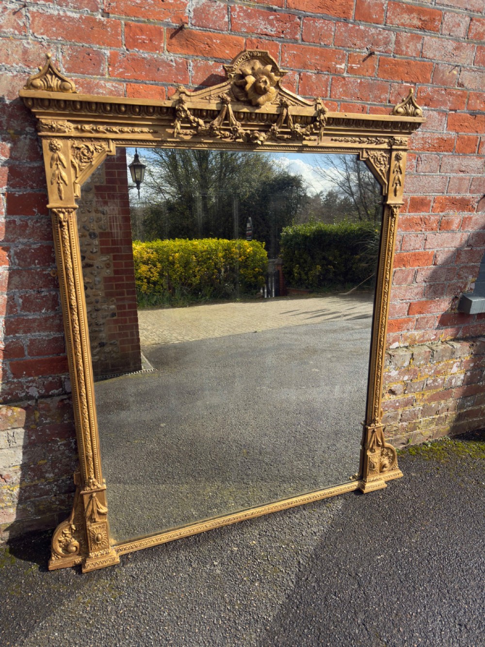A nineteenth-century giltwood overmantel mirror with detailed gesso moulding, corner spandrels, and a central carved floral cresting.
