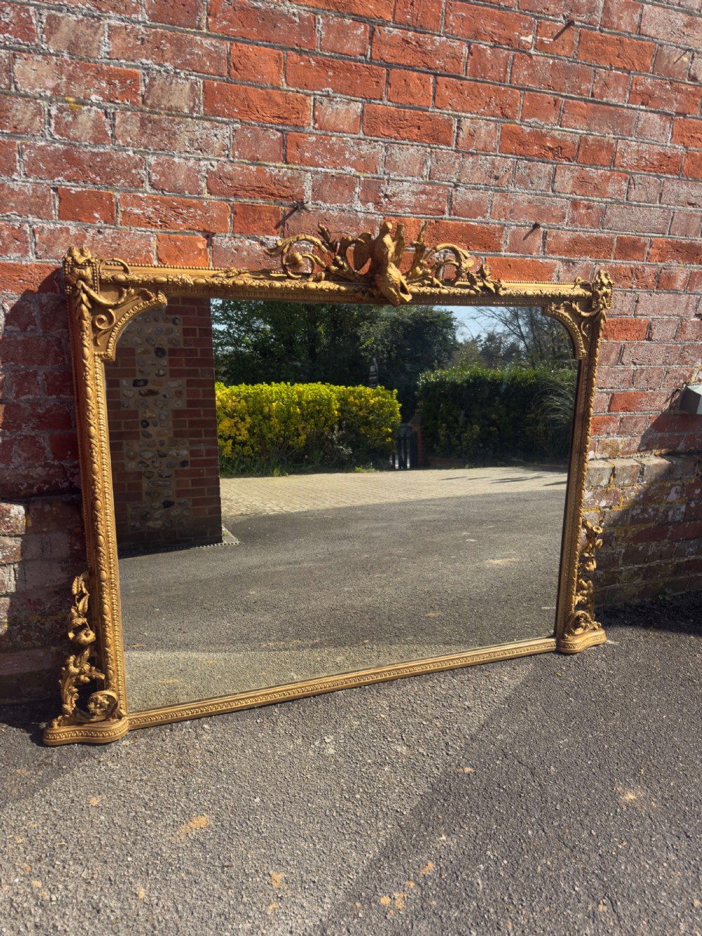A large nineteenth-century rectangular giltwood overmantel mirror featuring ornate cresting with a bird motif and scrolled foliate moulding along the frame.