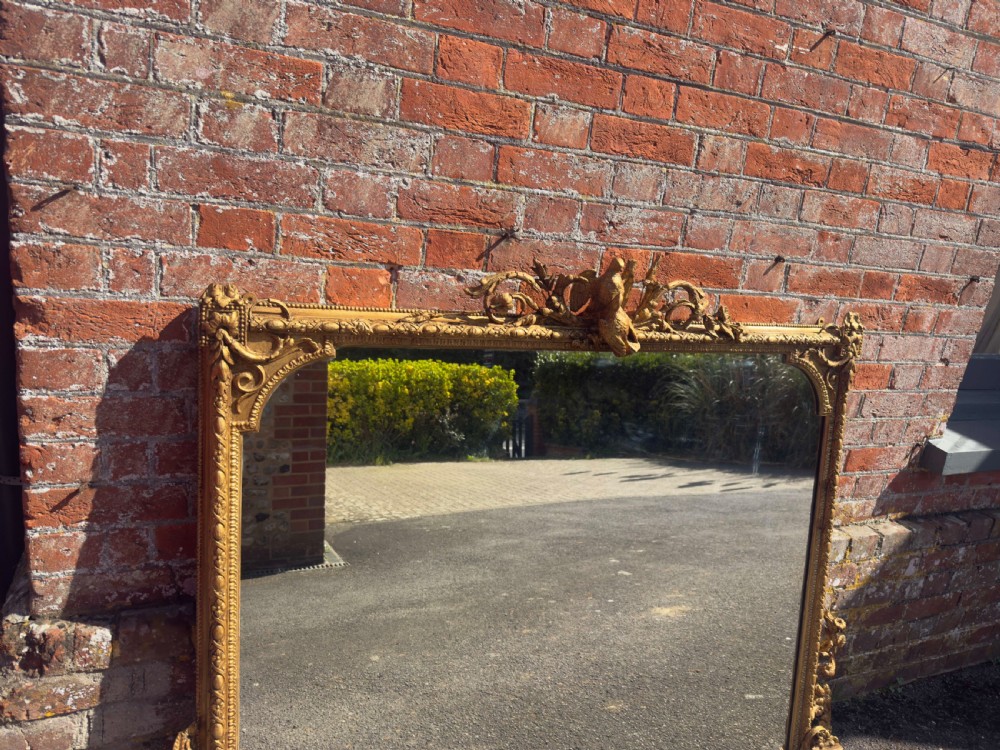 A large nineteenth-century rectangular giltwood overmantel mirror featuring ornate cresting with a bird motif and scrolled foliate moulding along the frame. View VI