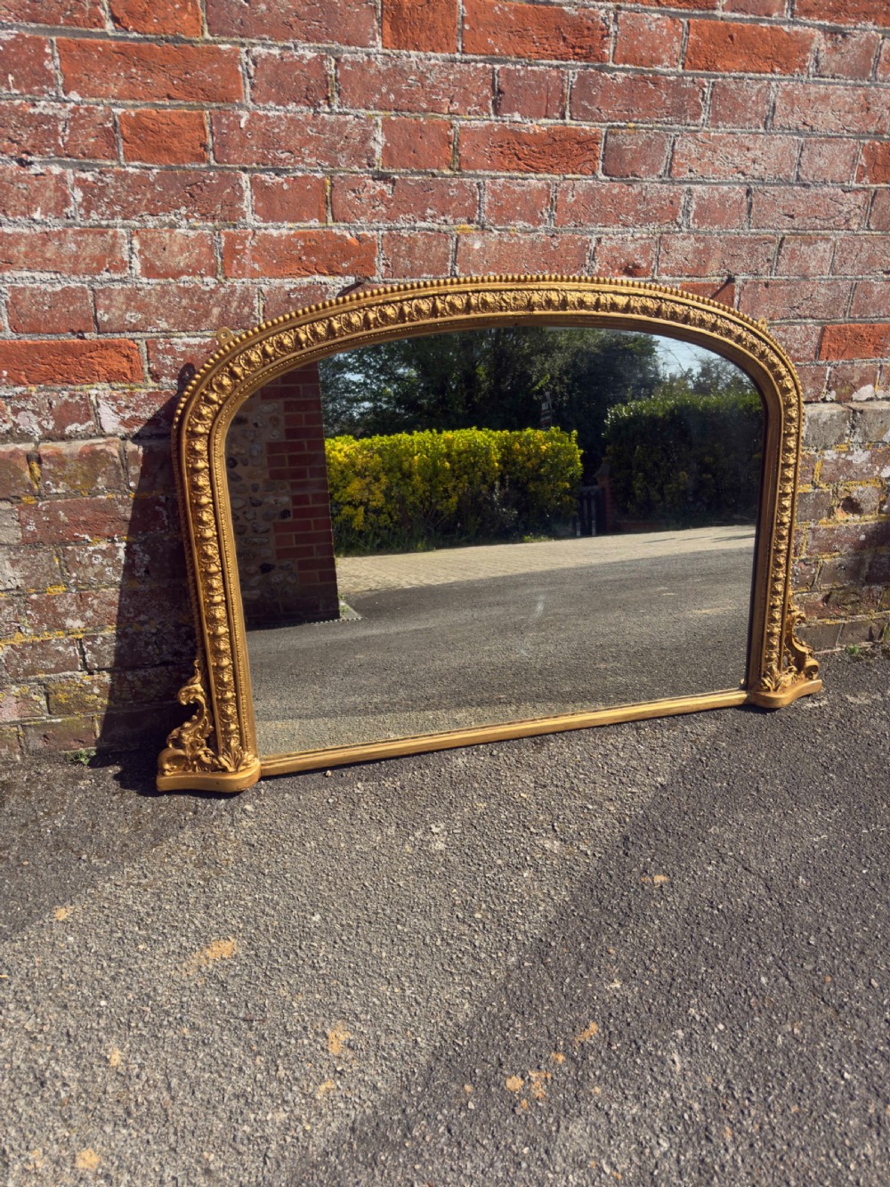 A 19th-century Victorian arched overmantel mirror featuring a gilded wood and gesso frame with carved bead detailing and ornate side flourishes.