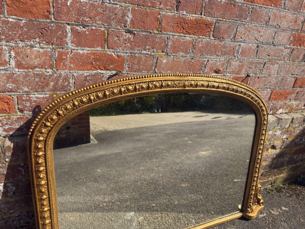 A 19th-century Victorian arched overmantel mirror featuring a gilded wood and gesso frame with carved bead detailing and ornate side flourishes. View II