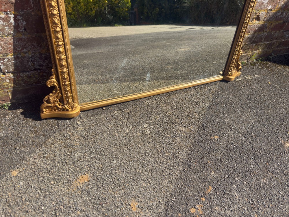 A 19th-century Victorian arched overmantel mirror featuring a gilded wood and gesso frame with carved bead detailing and ornate side flourishes. View VI