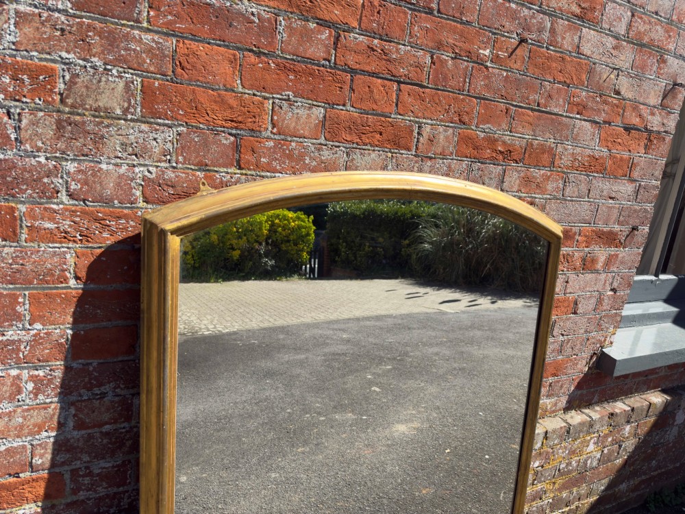 A large nineteenth-century English overmantel mirror featuring a gilded wood and gesso frame with an arched top and moulded edges. View III