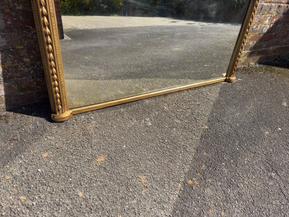 A large nineteenth-century English overmantel mirror featuring a gilded wood and gesso frame with an arched top and moulded edges. View VI