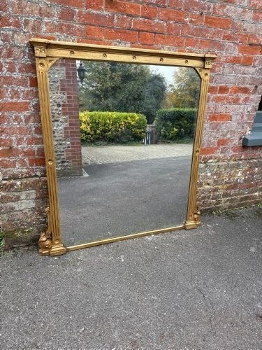 A large 19th-century English giltwood overmantel mirror featuring ribbed pilasters and rosette carvings around a rectangular mirror glass plate.