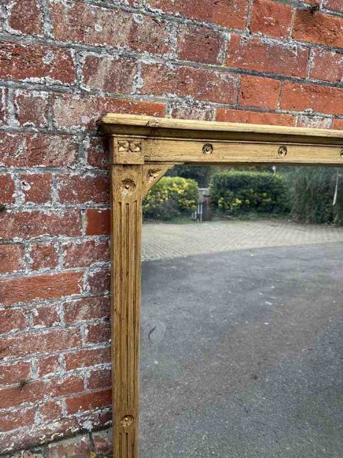 A large 19th-century English giltwood overmantel mirror featuring ribbed pilasters and rosette carvings around a rectangular mirror glass plate. View II