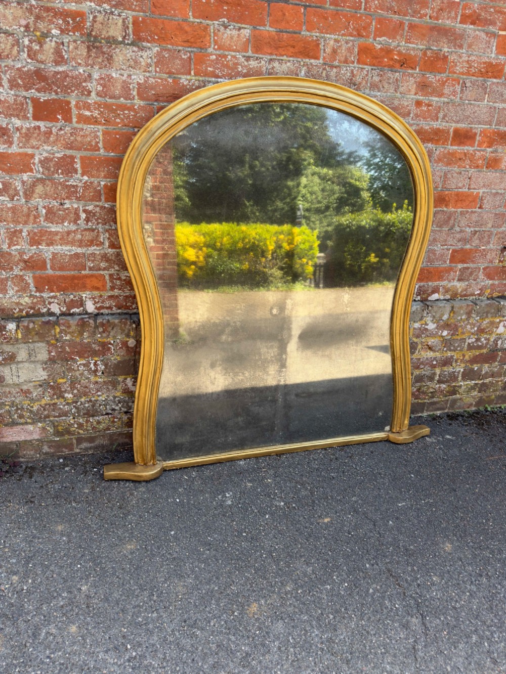 A 19th-century English giltwood overmantel mirror featuring an arched hourglass shape with small side foot supports.