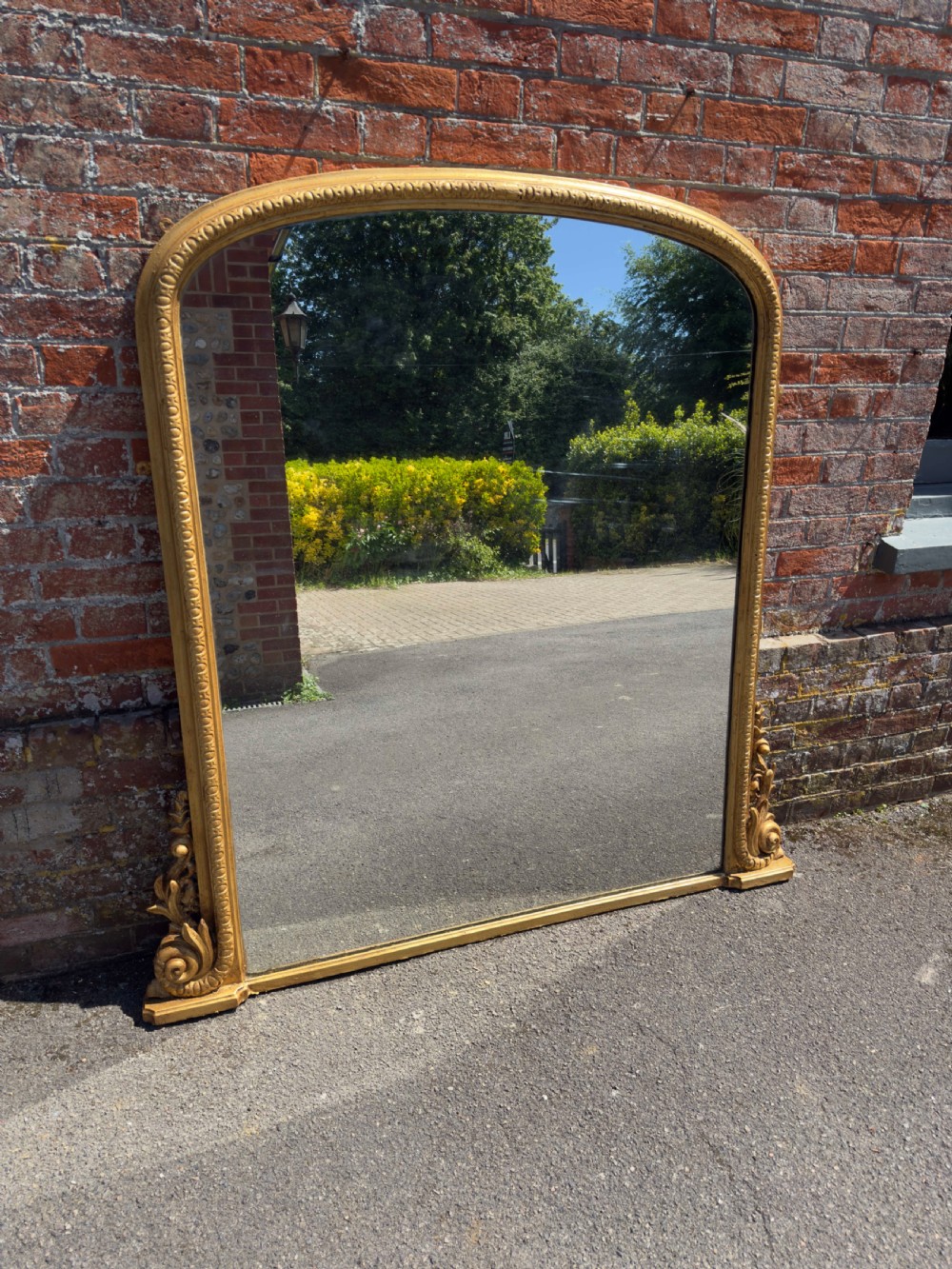 A 19th-century English giltwood overmantel mirror featuring an arched top frame and carved acanthus leaf details at the base.