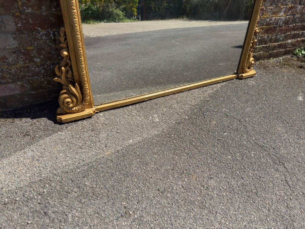 A 19th-century English giltwood overmantel mirror featuring an arched top frame and carved acanthus leaf details at the base. View V