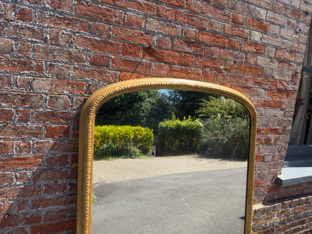 A 19th-century English giltwood overmantel mirror featuring an arched top frame and carved acanthus leaf details at the base. View VII