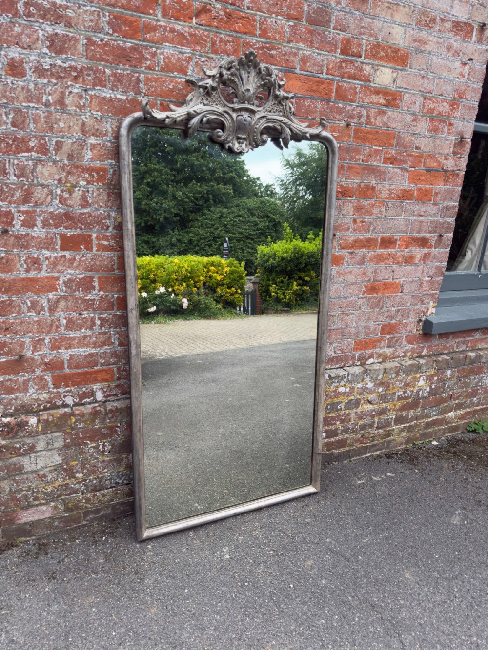 A tall 19th-century French arched mirror with a carved foliate gesso crest and aged silver leaf finish.