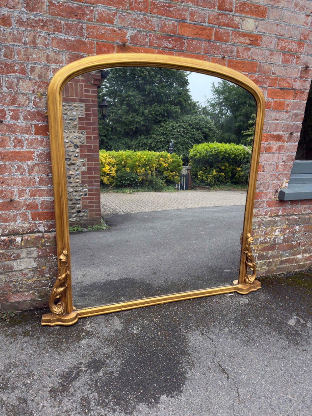 A large 19th-century English overmantel mirror with an arched gold giltwood and gesso frame featuring carved scroll motifs at the base.