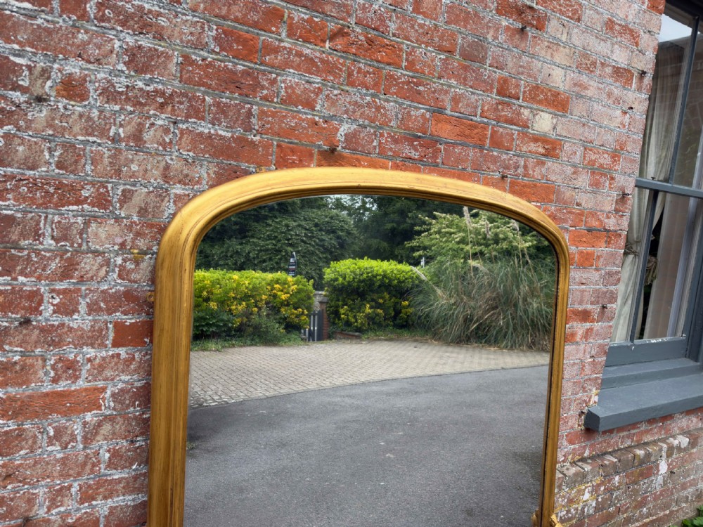 A large 19th-century English overmantel mirror with an arched gold giltwood and gesso frame featuring carved scroll motifs at the base. View II