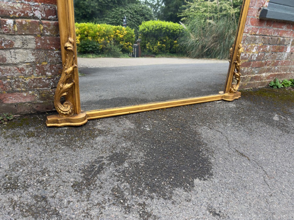 A large 19th-century English overmantel mirror with an arched gold giltwood and gesso frame featuring carved scroll motifs at the base. View III