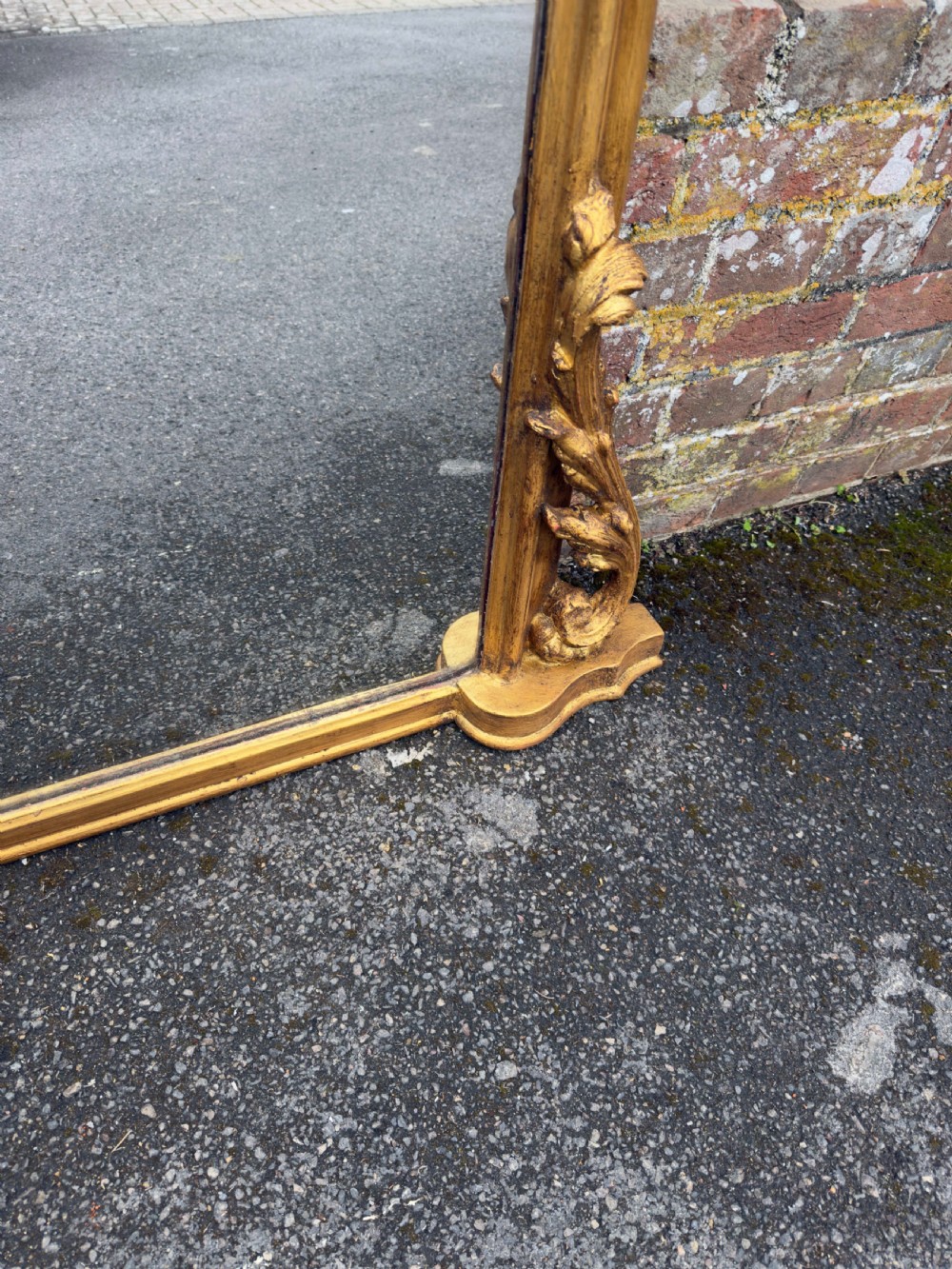 A large 19th-century English overmantel mirror with an arched gold giltwood and gesso frame featuring carved scroll motifs at the base. View IV