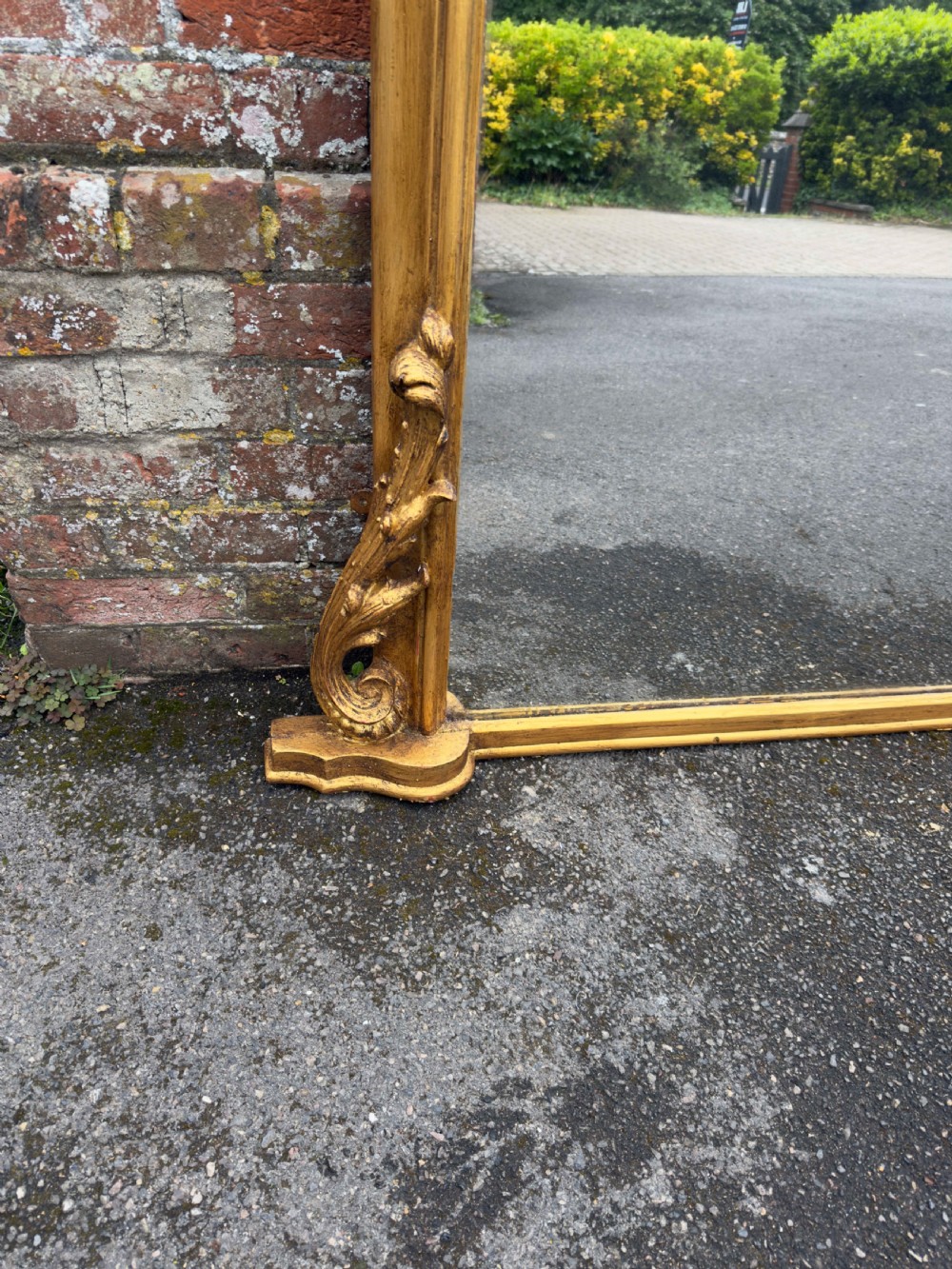 A large 19th-century English overmantel mirror with an arched gold giltwood and gesso frame featuring carved scroll motifs at the base. View V