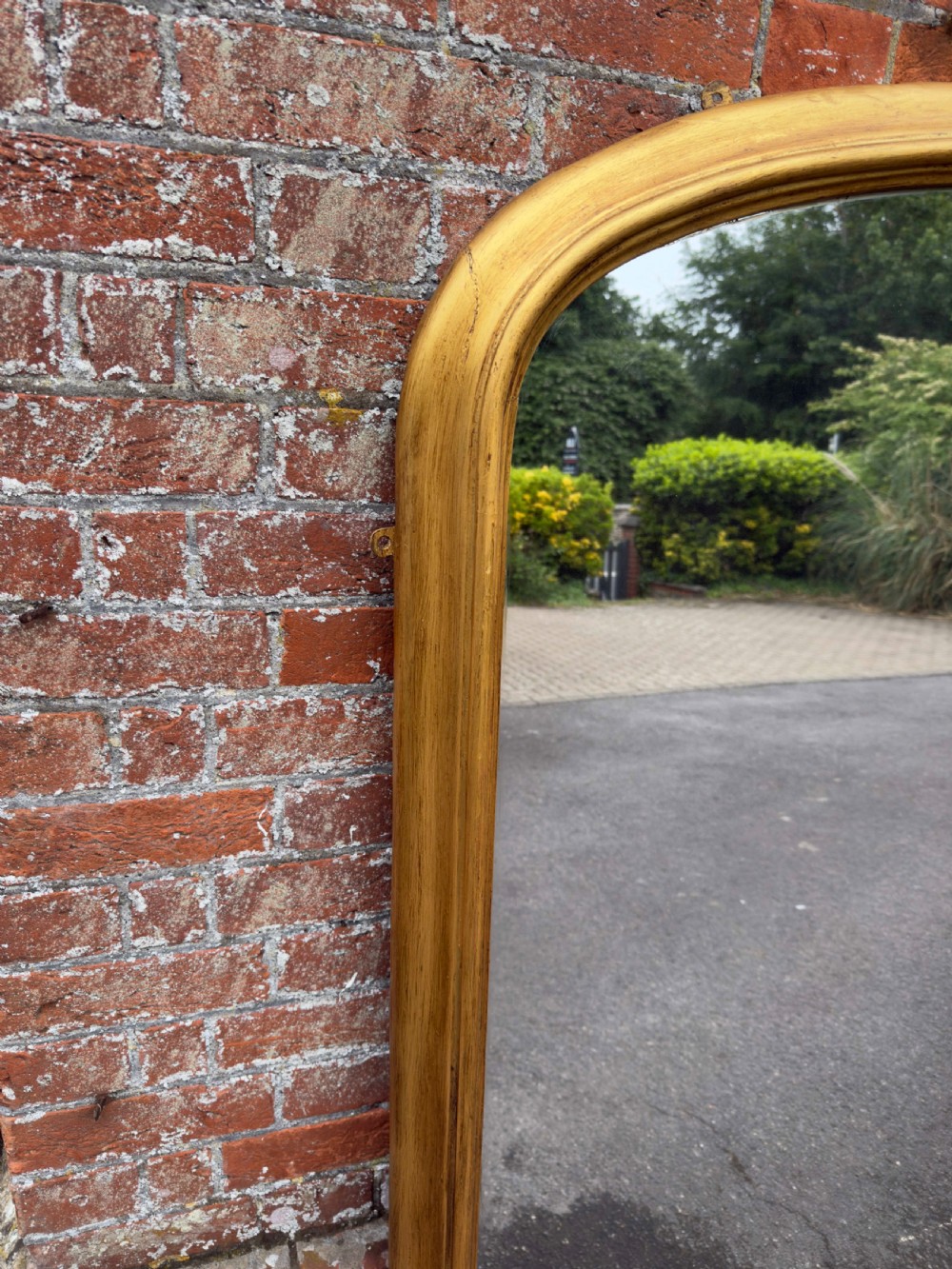 A large 19th-century English overmantel mirror with an arched gold giltwood and gesso frame featuring carved scroll motifs at the base. View VI